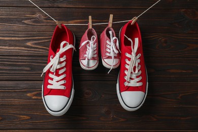 Photo of Big and small sneakers hanging on wooden background