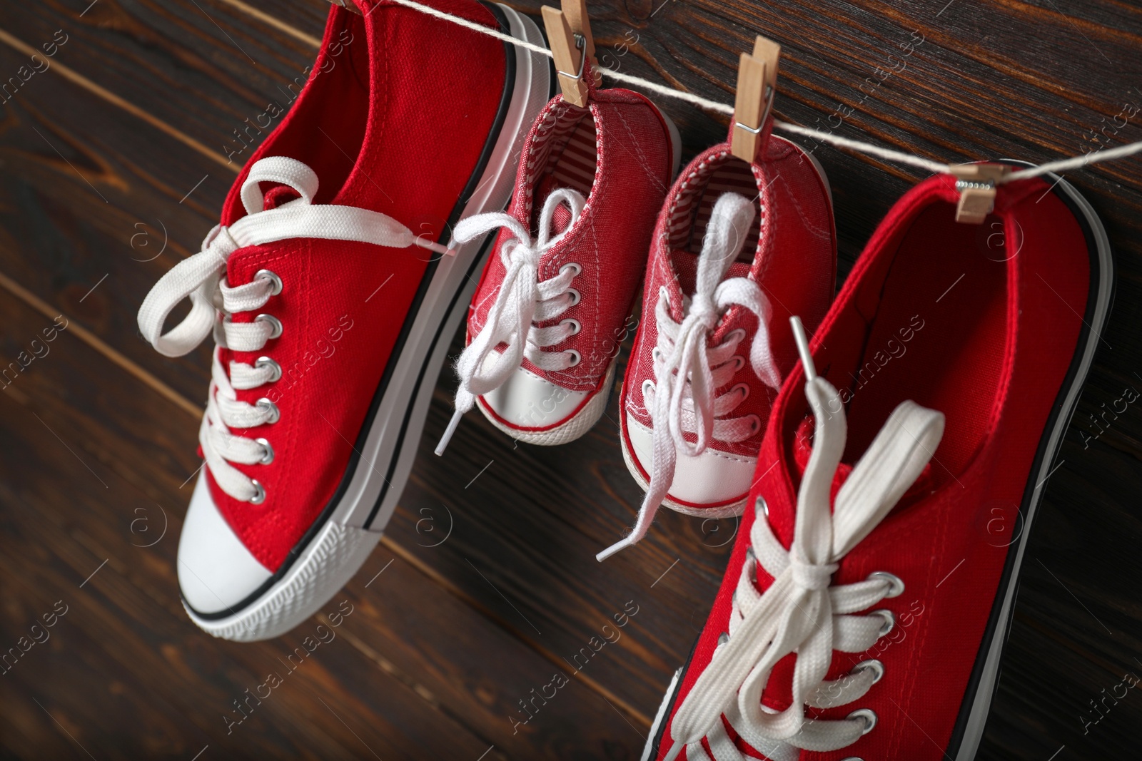 Photo of Big and small sneakers hanging on wooden background