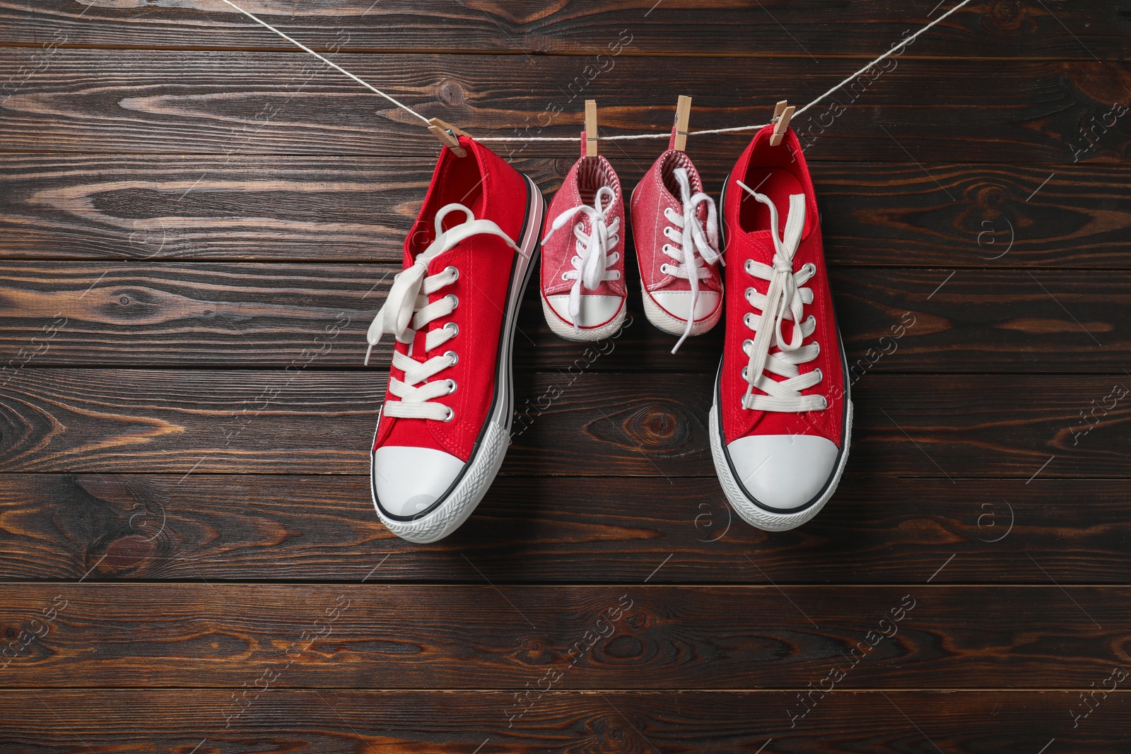 Photo of Big and small sneakers hanging on wooden background