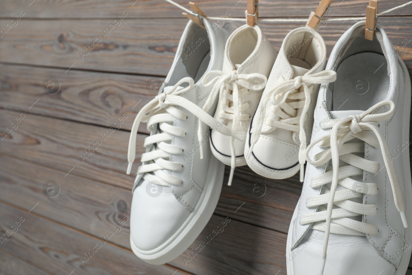 Photo of Big and small sneakers hanging on wooden background