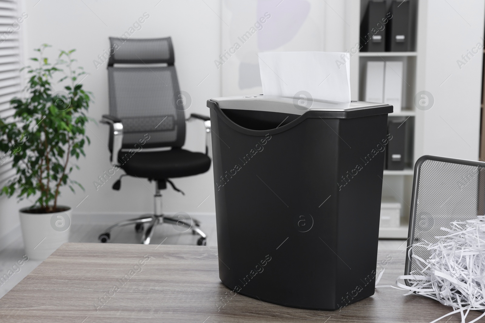 Photo of Destroying sheets of paper with shredder on wooden table in office