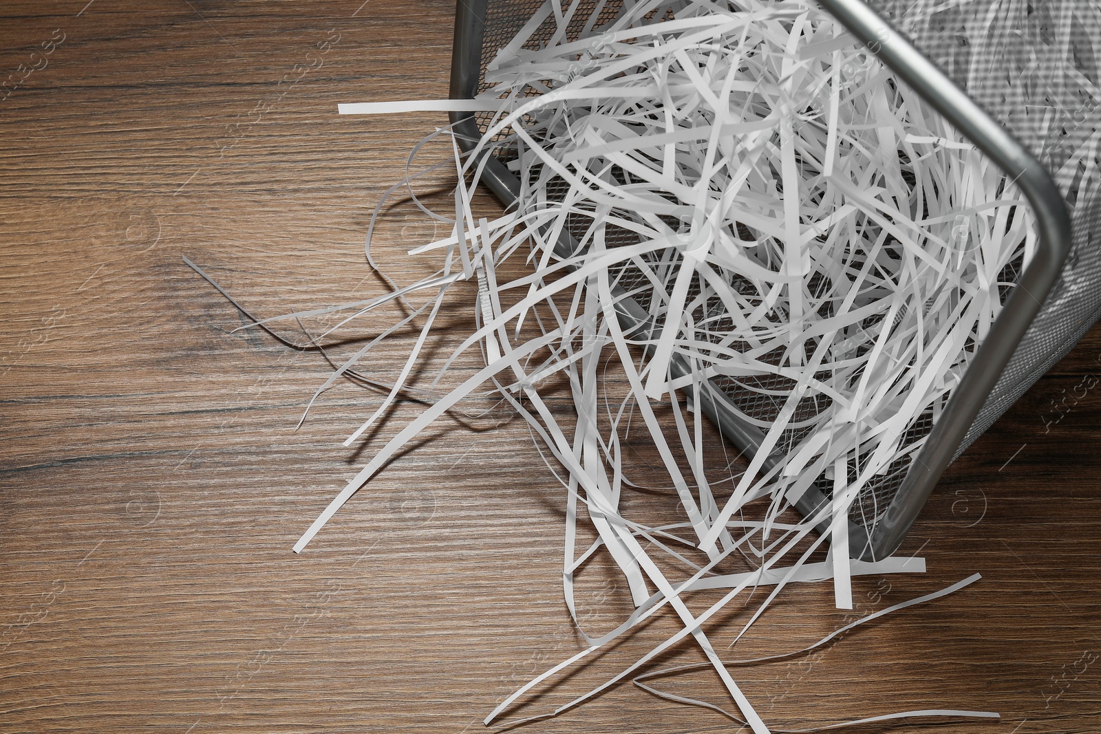 Photo of Shredded paper strips in trash bin on wooden table