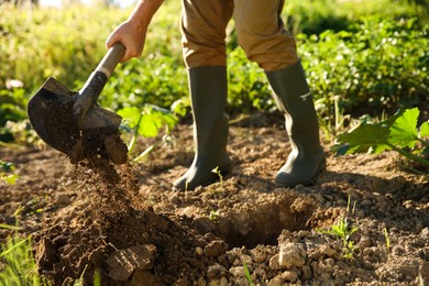 Photo of Farmer digging soil with shovel on sunny day, closeup