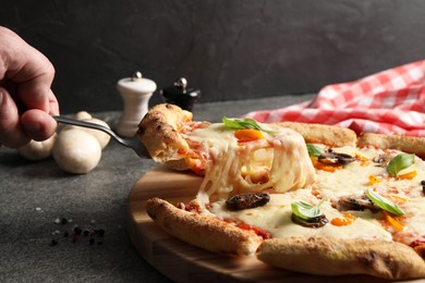 Photo of Man taking piece of delicious vegetarian pizza at grey table, closeup