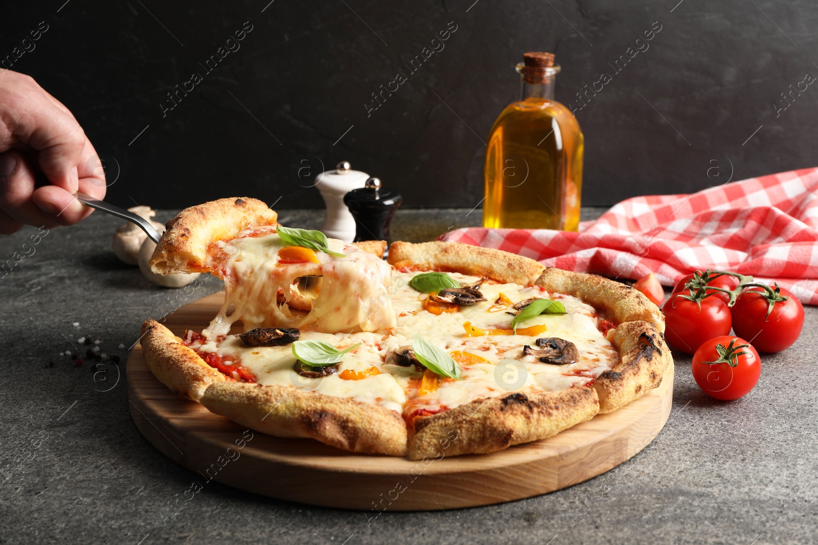 Photo of Man taking piece of delicious vegetarian pizza at grey table, closeup