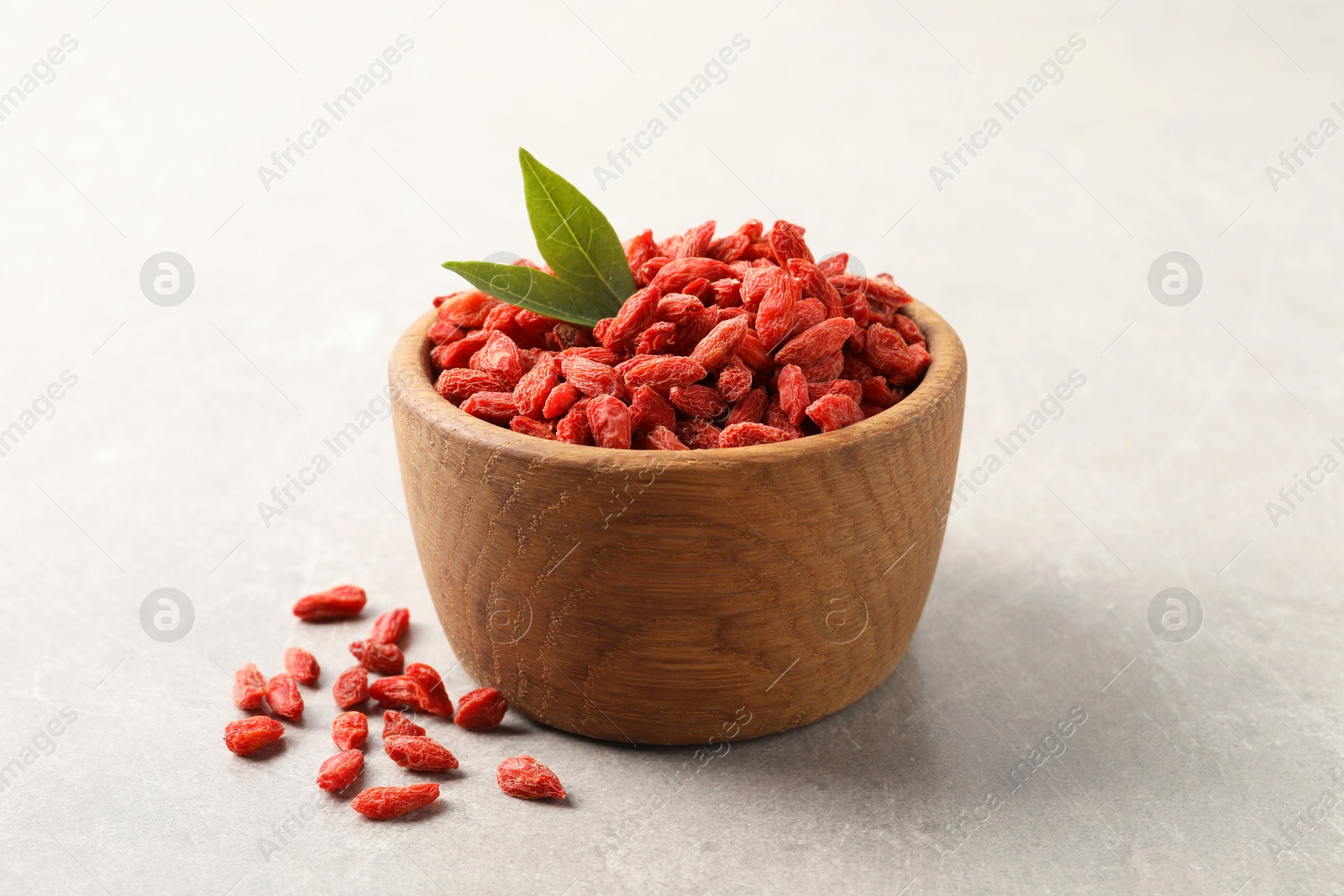 Photo of Dried goji berries in bowl and green leaves on light grey table