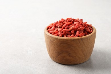 Dried goji berries in bowl on light grey table, space for text