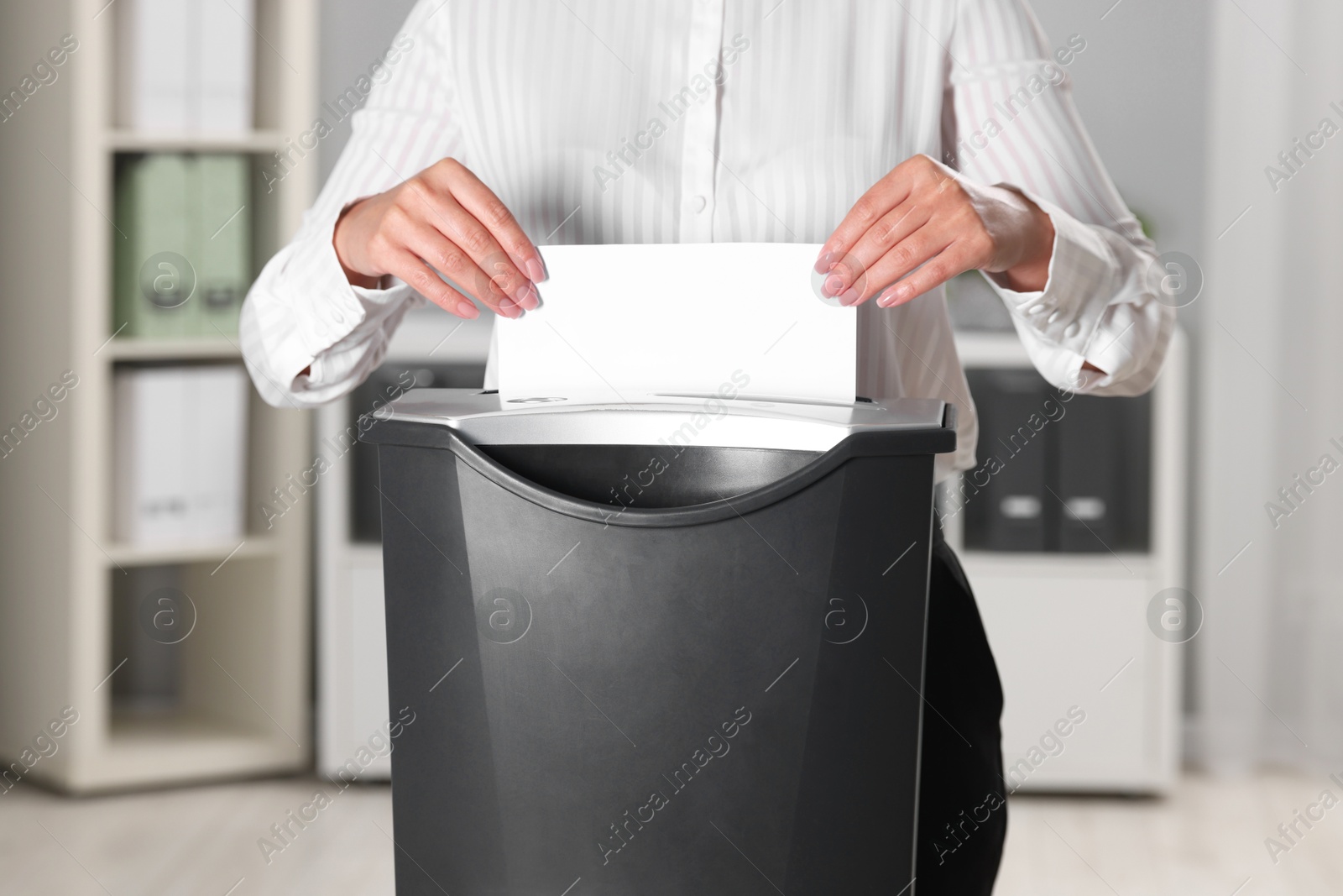 Photo of Woman destroying sheet of paper with shredder in office, closeup