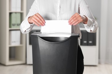 Woman destroying sheet of paper with shredder in office, closeup