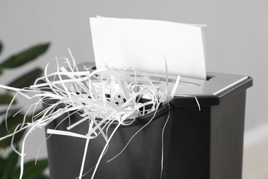 Photo of Destroying sheets of paper with shredder indoors, closeup