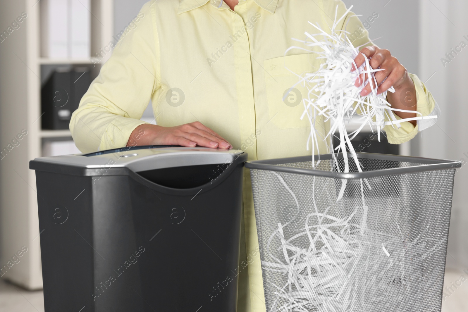 Photo of Woman putting shredded paper strips into trash bin in office, closeup