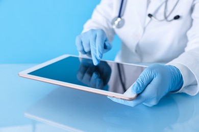 Photo of Doctor with tablet at table against light blue background, closeup view