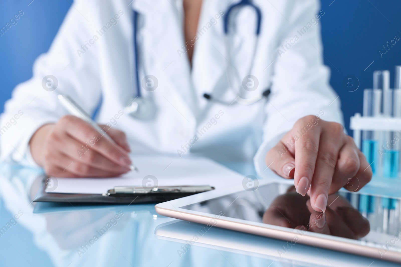 Photo of Doctor with tablet at table against blue background, closeup view