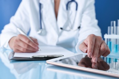 Photo of Doctor with tablet at table against blue background, closeup view