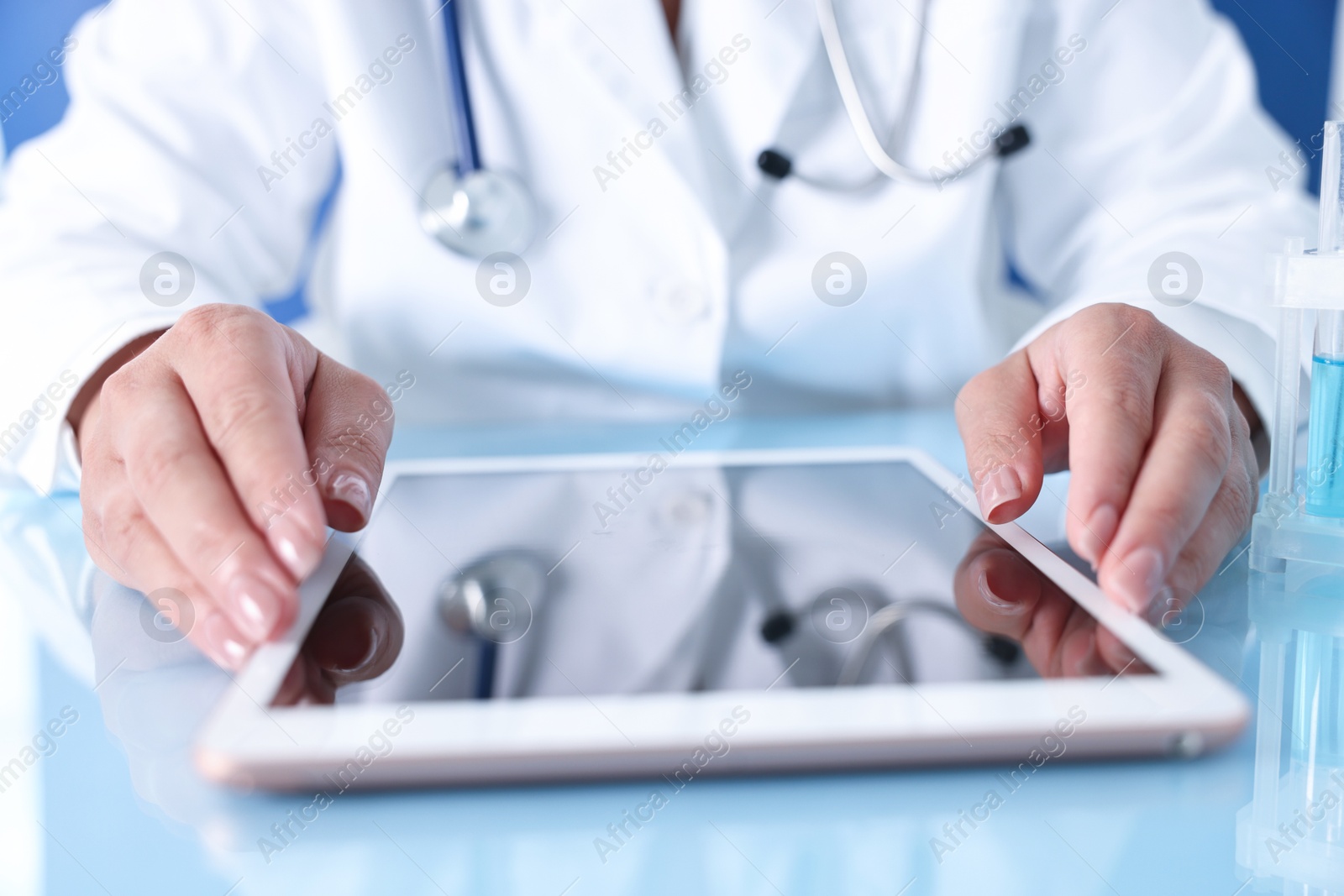 Photo of Doctor with tablet at table against blue background, closeup view