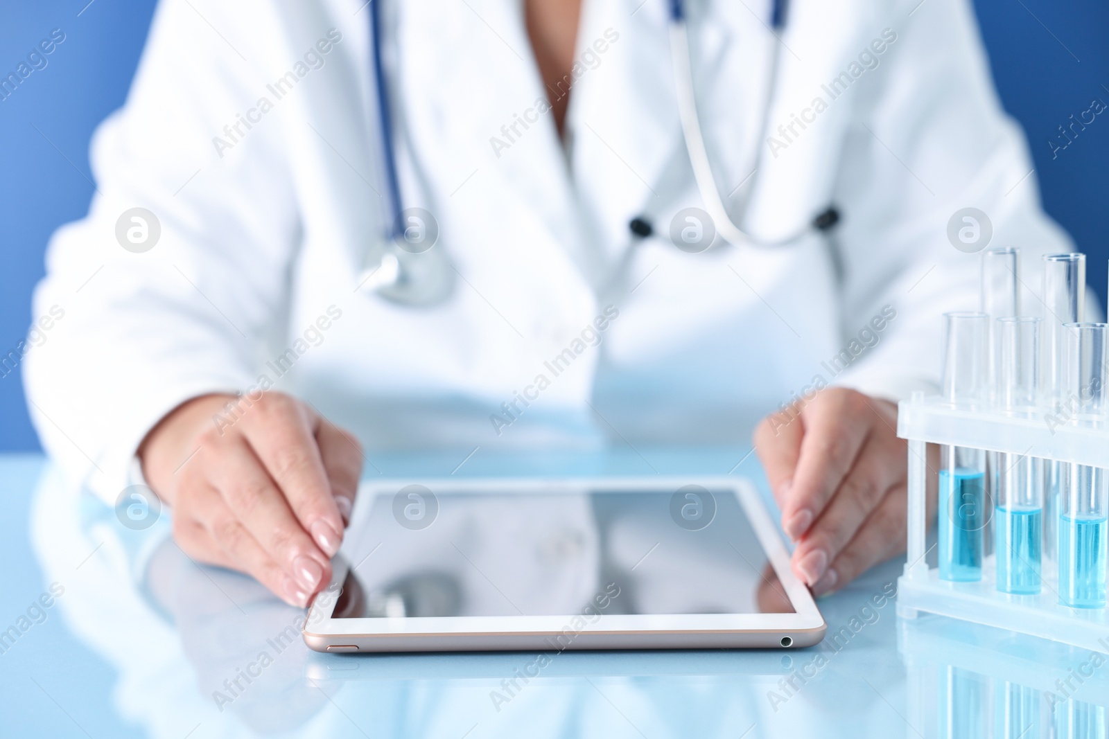 Photo of Doctor with tablet at table against blue background, closeup view