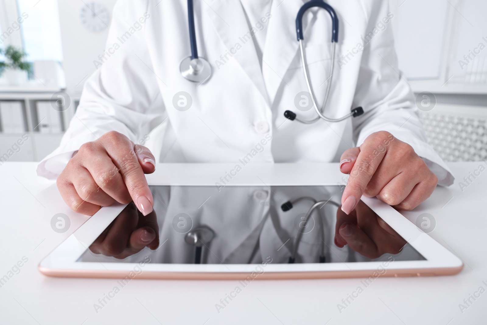 Photo of Doctor with tablet at table in clinic, closeup view