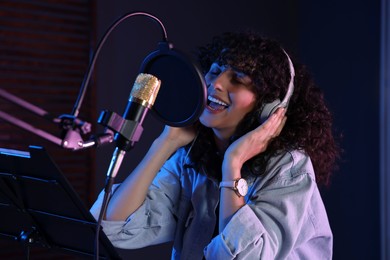 Photo of Vocalist with headphones singing into microphone in professional record studio