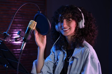 Photo of Singer wearing headphones with microphone singing in professional record studio