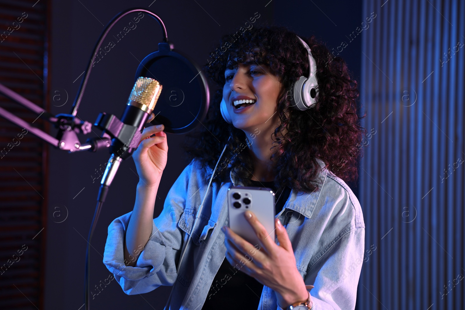 Photo of Vocalist with smartphone singing into microphone in professional record studio