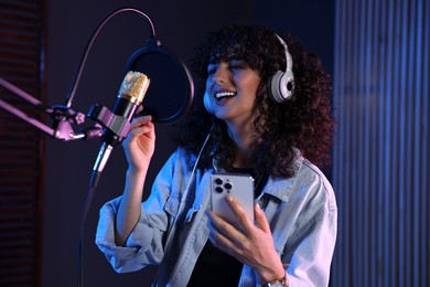 Vocalist with smartphone singing into microphone in professional record studio