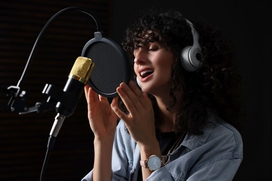 Photo of Vocalist with headphones singing into microphone in professional record studio