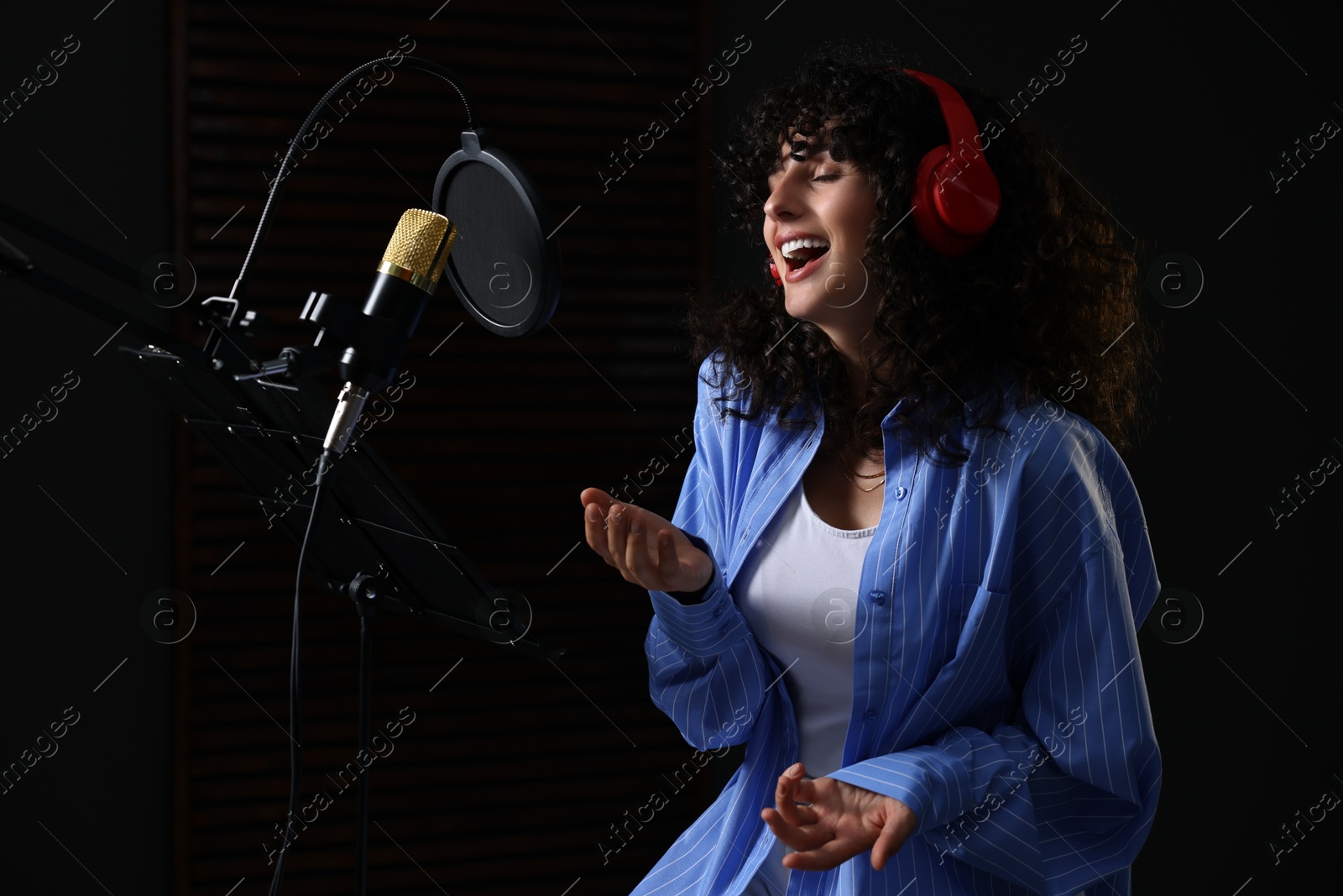 Photo of Vocalist with headphones singing into microphone in professional record studio