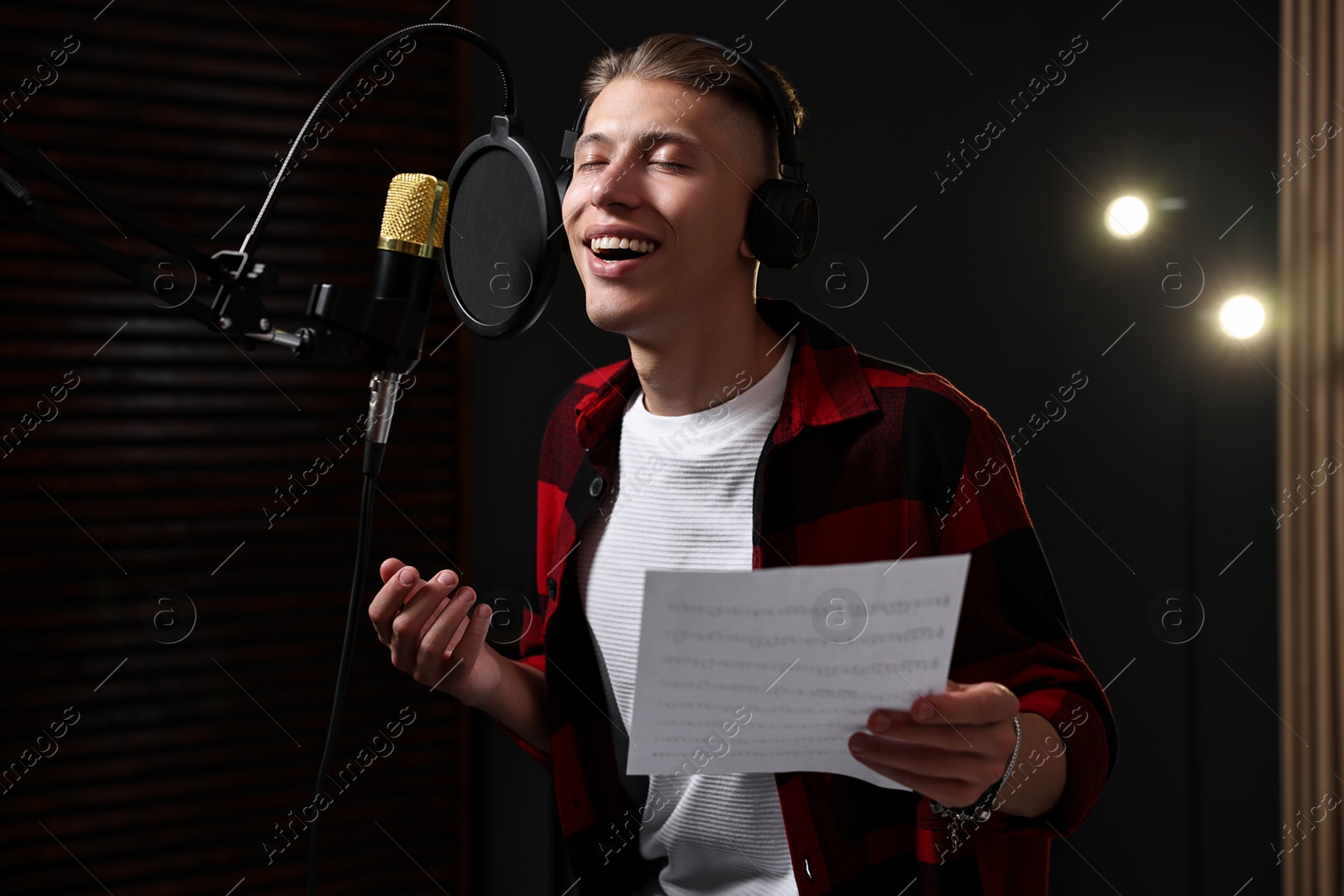 Photo of Singer with sheet recording song in professional studio