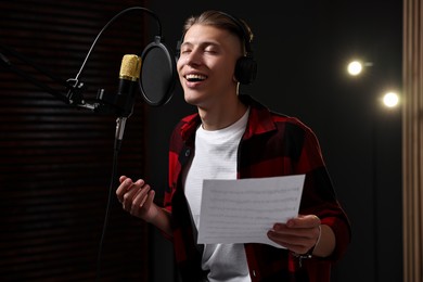 Photo of Singer with sheet recording song in professional studio