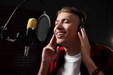 Photo of Singer with headphones recording song in professional studio