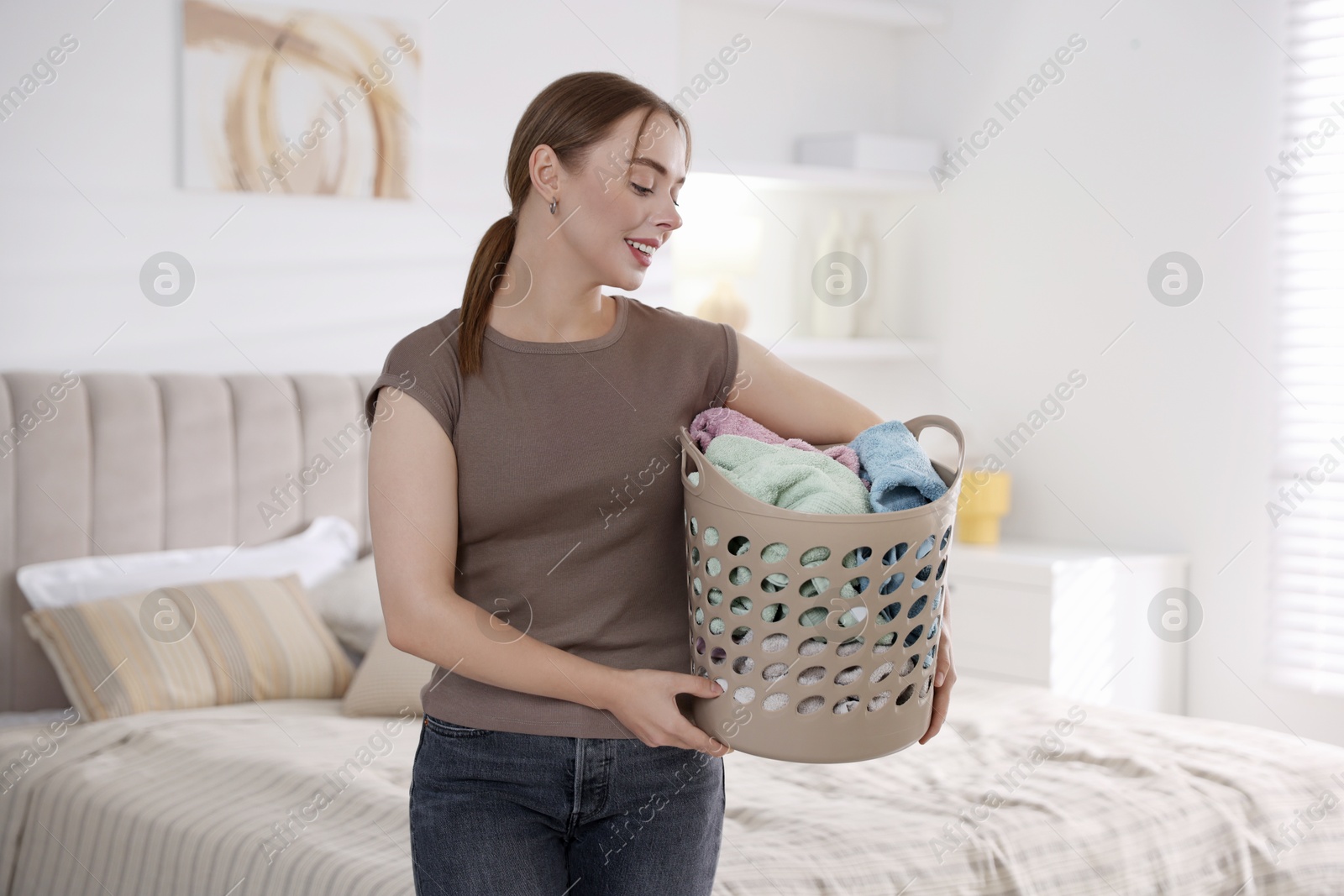 Photo of Happy young housewife with basket full of laundry at home