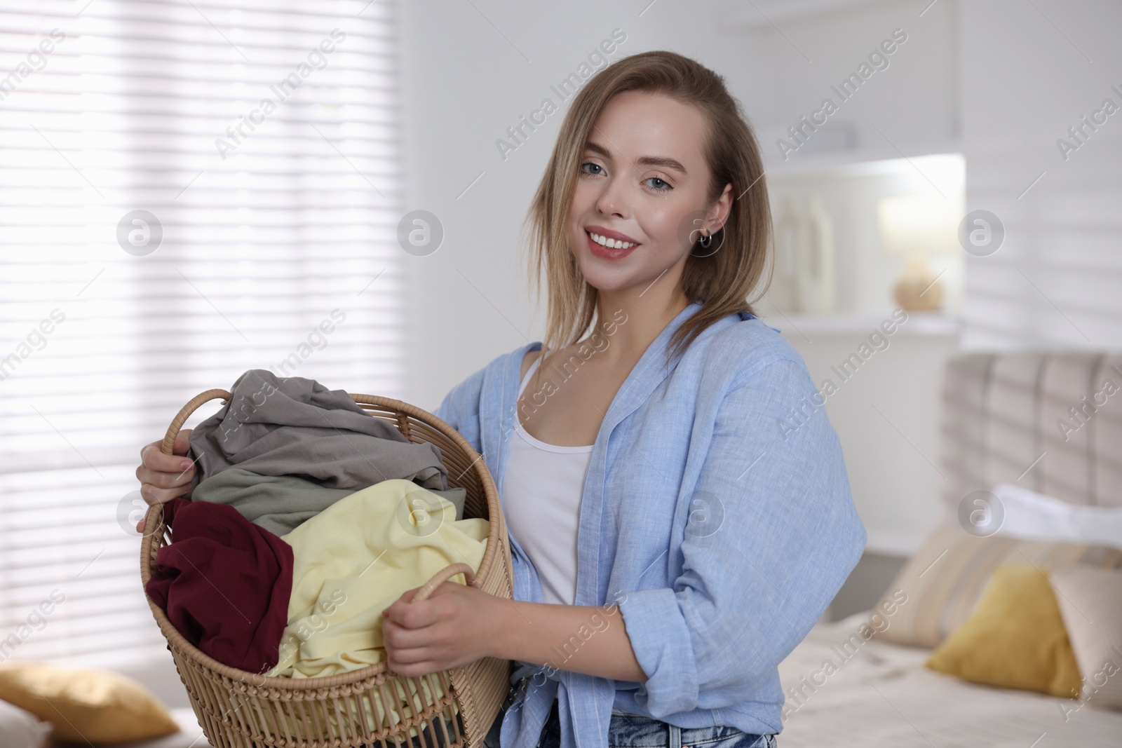 Photo of Happy young housewife with basket full of laundry at home