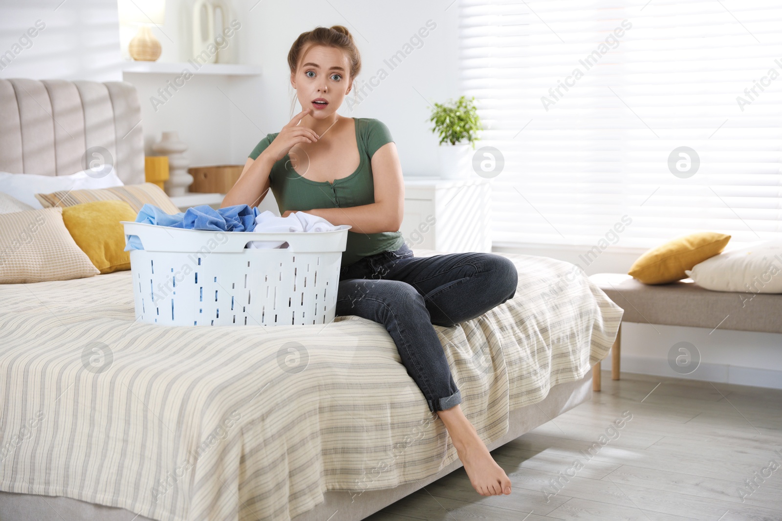 Photo of Emotional housewife with basket full of laundry on bed at home