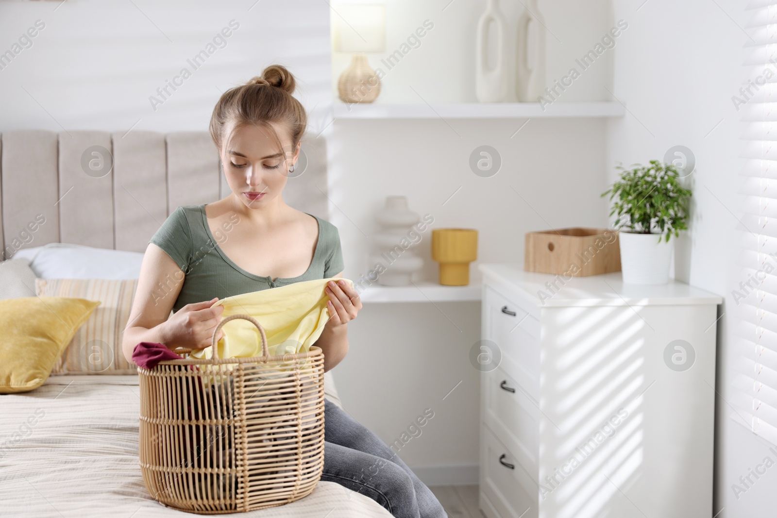 Photo of Young housewife with basket full of laundry on bed at home