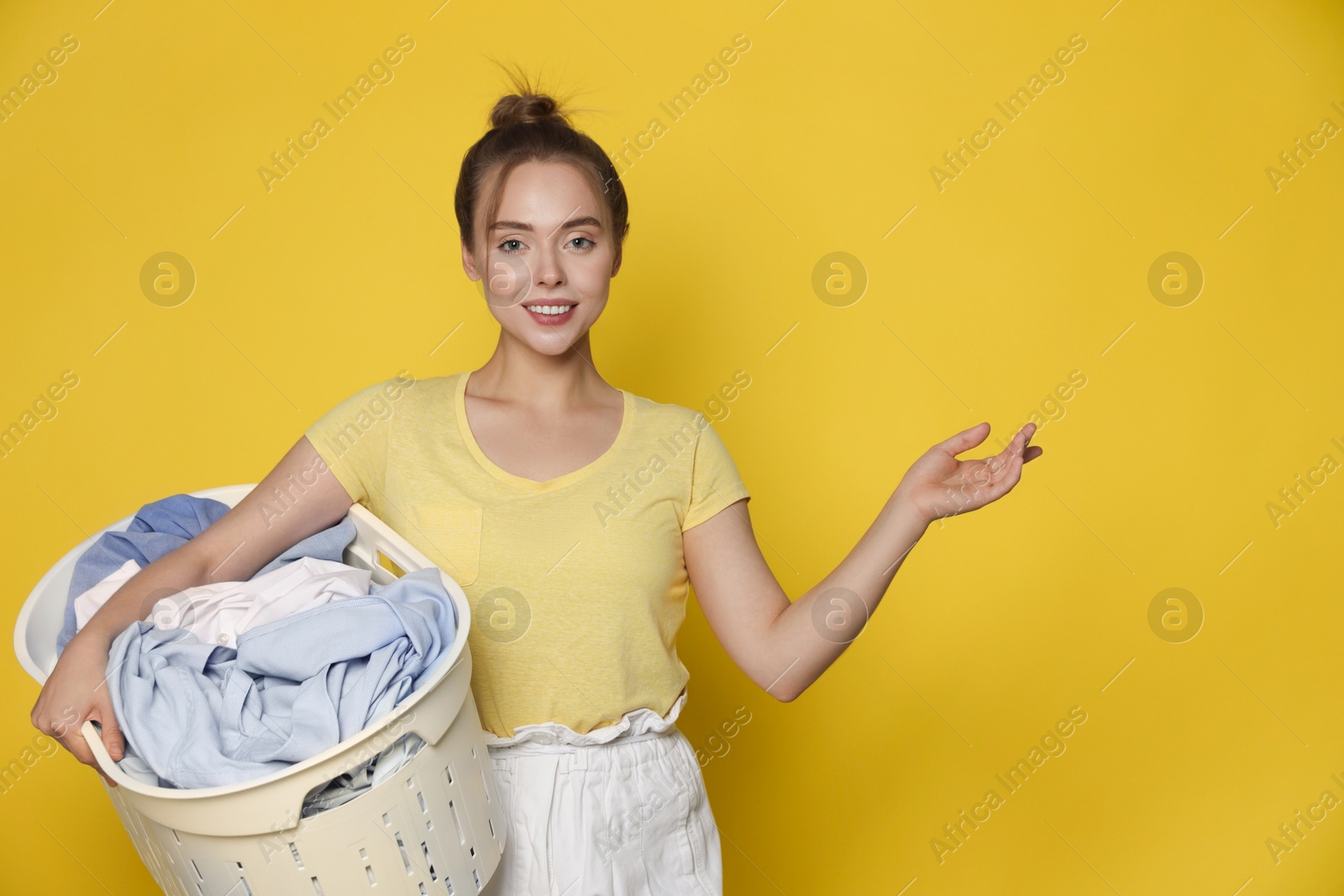 Photo of Happy young housewife with basket full of laundry on yellow background