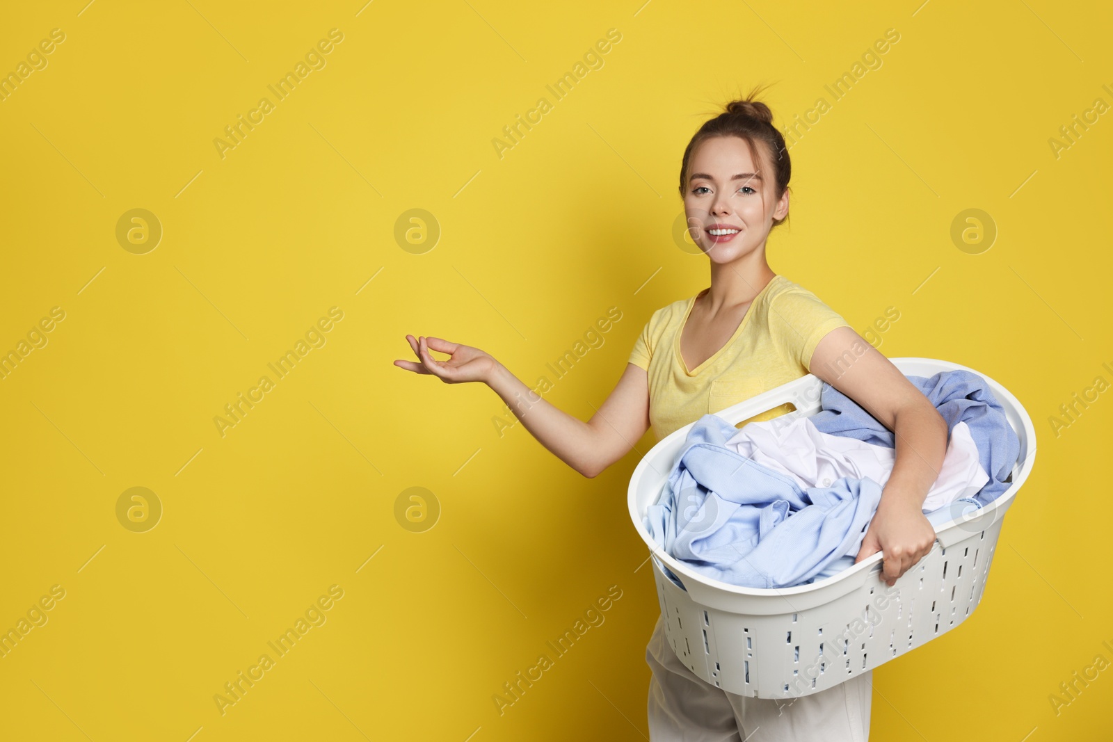 Photo of Happy young housewife with basket full of laundry on yellow background