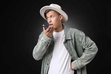 Young man recording voice message via smartphone on dark background