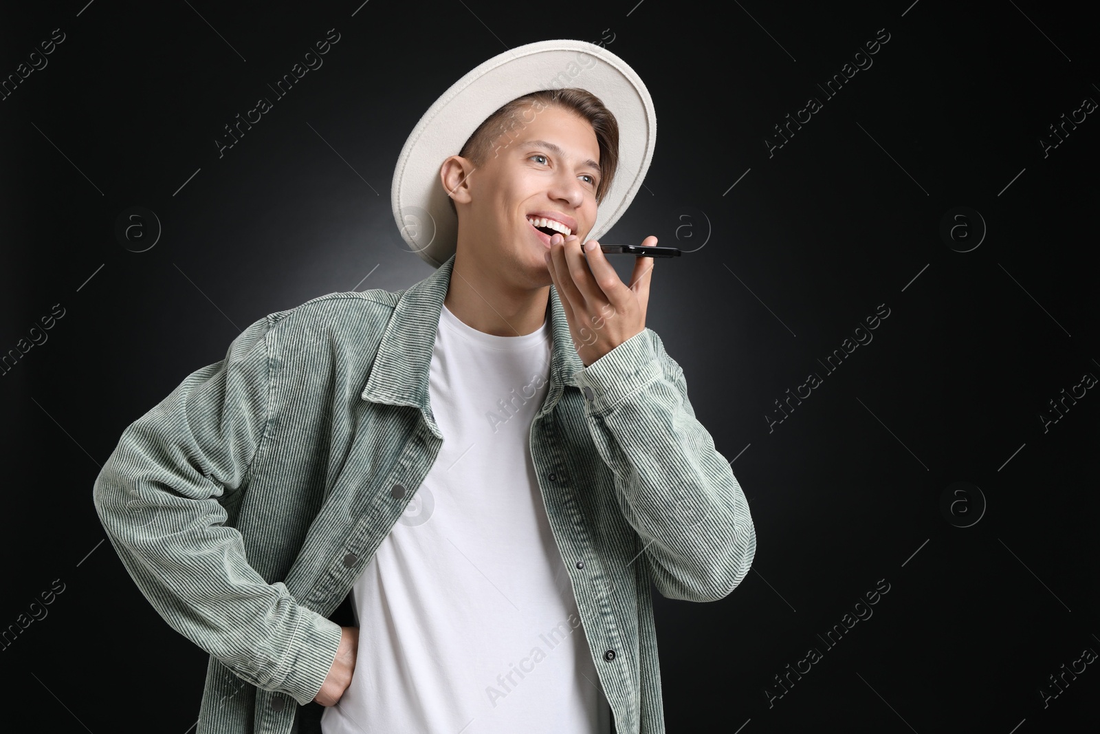 Photo of Young man recording voice message via smartphone on dark background