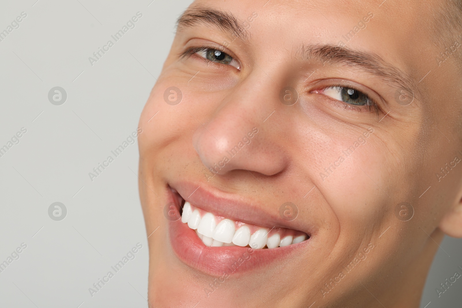 Photo of Happy young man on gray background, closeup. Dental veneers