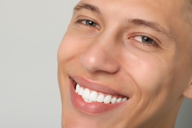 Happy young man on gray background, closeup. Dental veneers