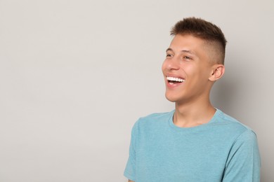 Happy young man on gray background, space for text. Dental veneers