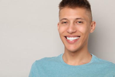 Happy young man on gray background, space for text. Dental veneers