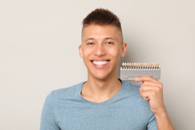 Happy young man with teeth color samples on gray background. Dental veneers