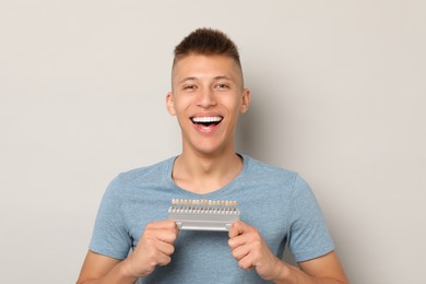 Happy young man with teeth color samples on gray background. Dental veneers