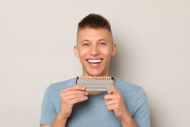 Photo of Happy young man with teeth color samples on gray background. Dental veneers