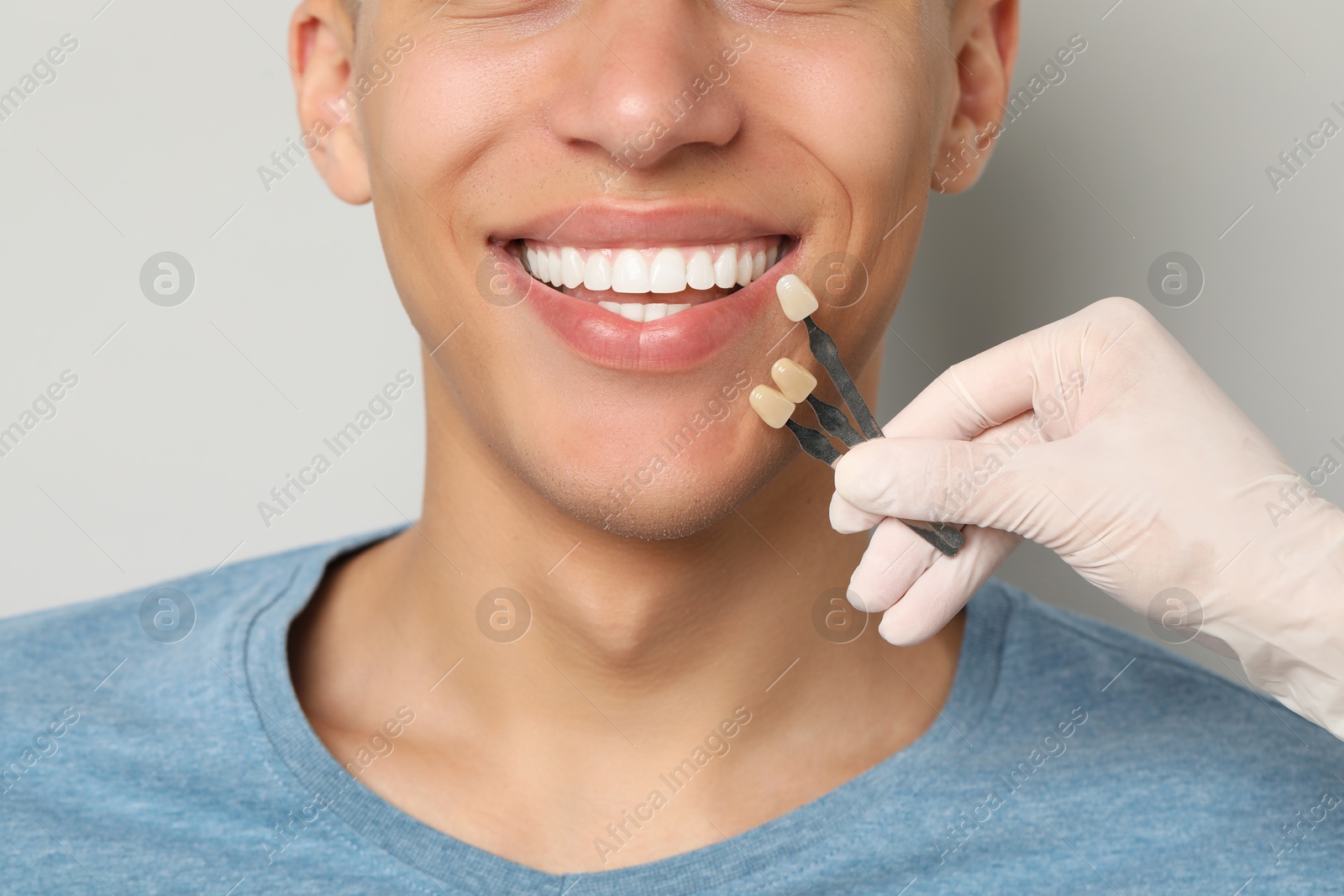 Photo of Doctor checking young man's teeth color on gray background, closeup. Dental veneers