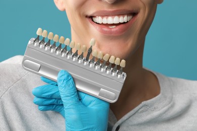 Photo of Doctor checking young man's teeth color on light blue background, closeup. Dental veneers