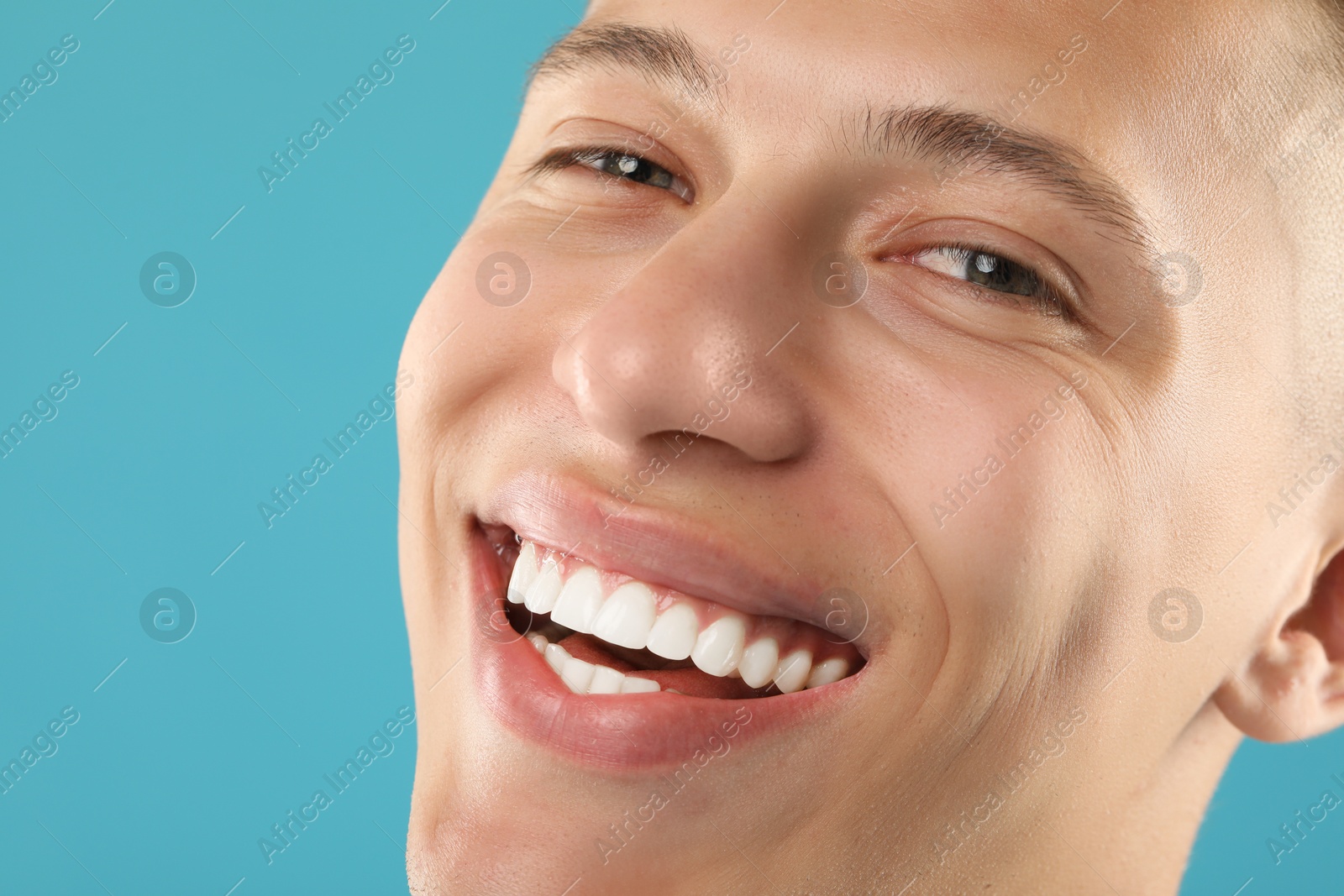 Photo of Happy young man on light blue background, closeup. Dental veneers