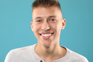 Photo of Happy young man on light blue background. Dental veneers