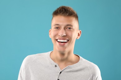 Happy young man on light blue background. Dental veneers